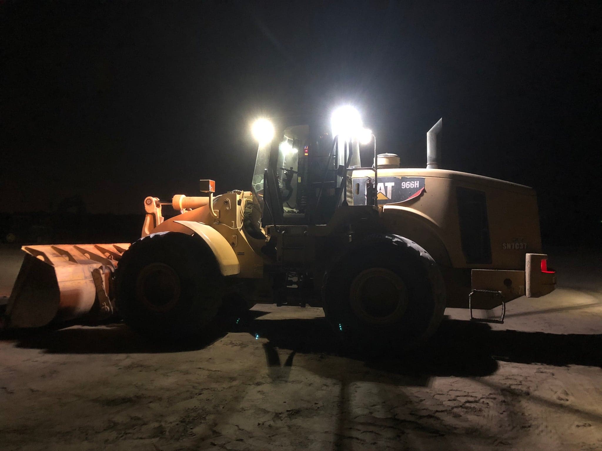 A Caterpillar 966H wheel loader working under its own lights after dark