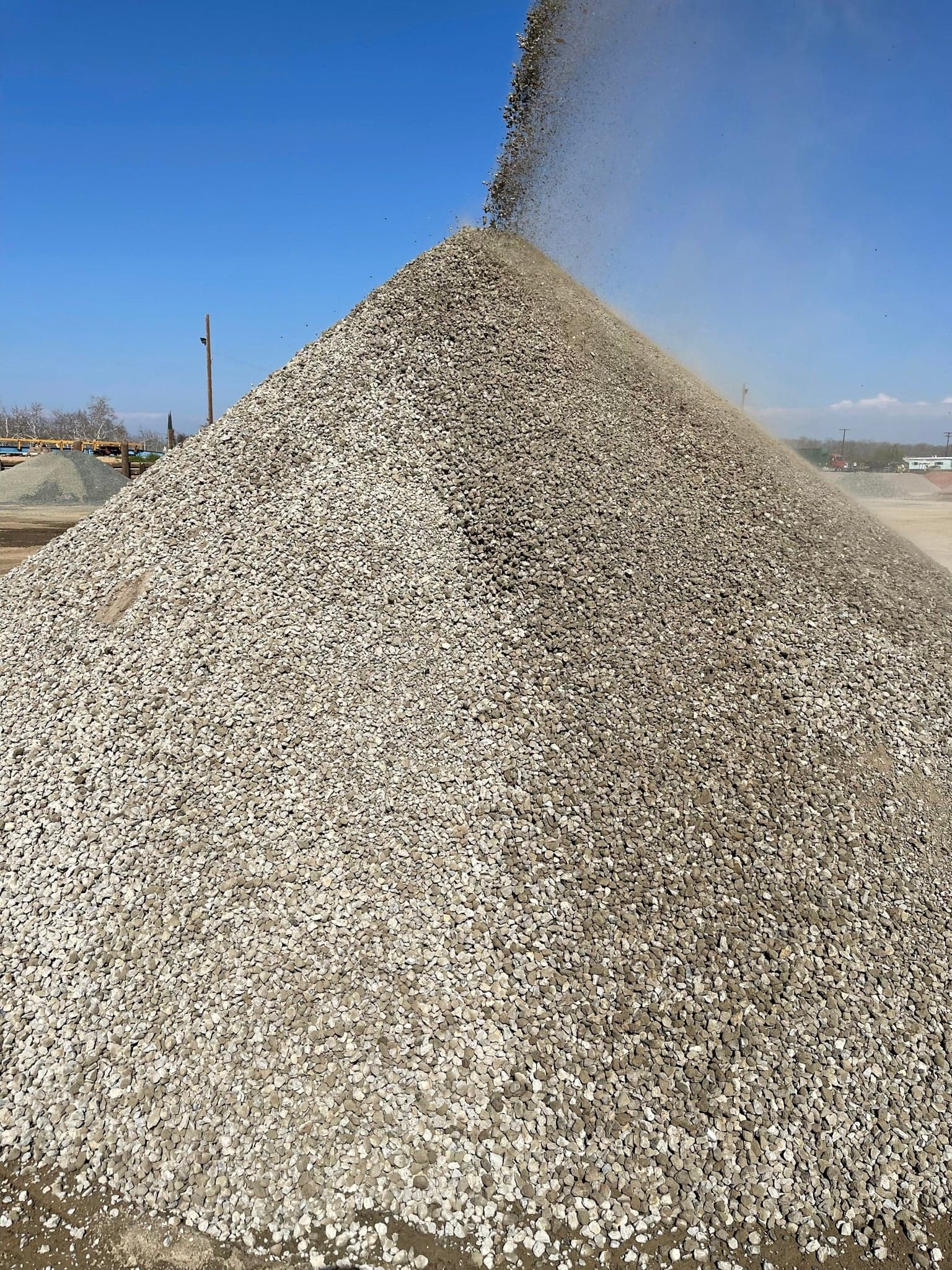 A tall cone-shaped stockpile of finished crushed rock building up under the crusher conveyor